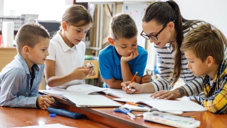 Teacher assisting a group of young students in a classroom, emphasising the importance of first aid for teachers in creating a safe learning environment.
