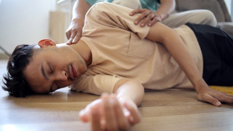 Person in recovery position after a seizure, with someone providing assistance — demonstrating the importance of a seizure first aid kit during a medical emergency.